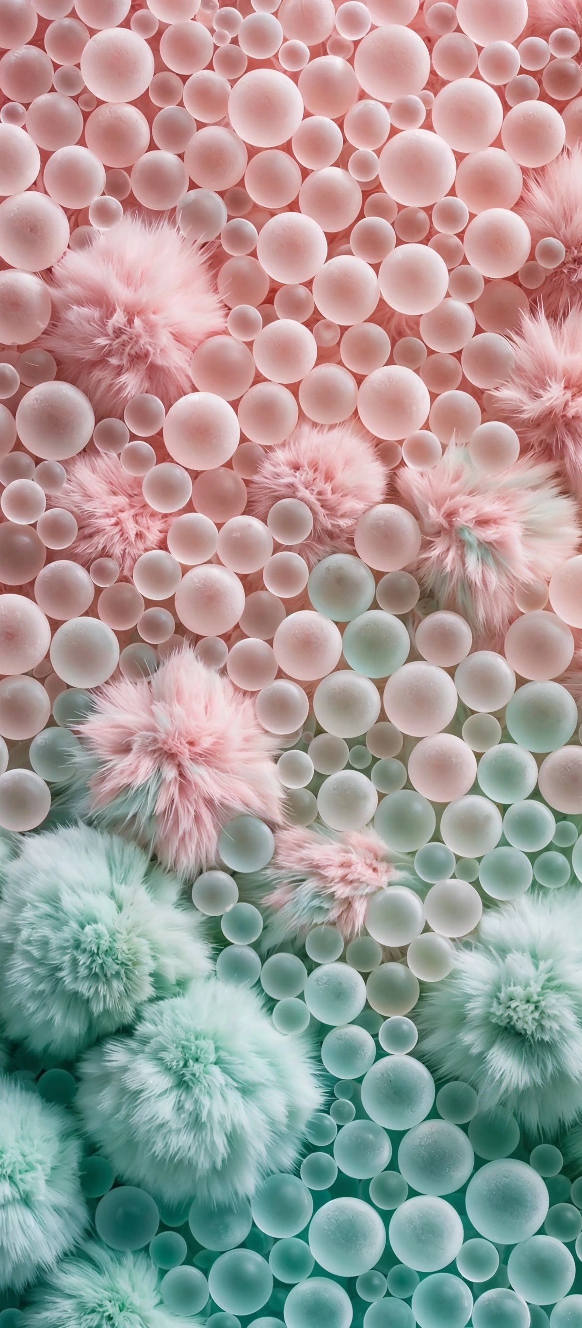 Overhead view of pink and mint green fluffy pompoms interspersed with clear and frosted glass or plastic spheres of different sizes arranged in a gradient pattern