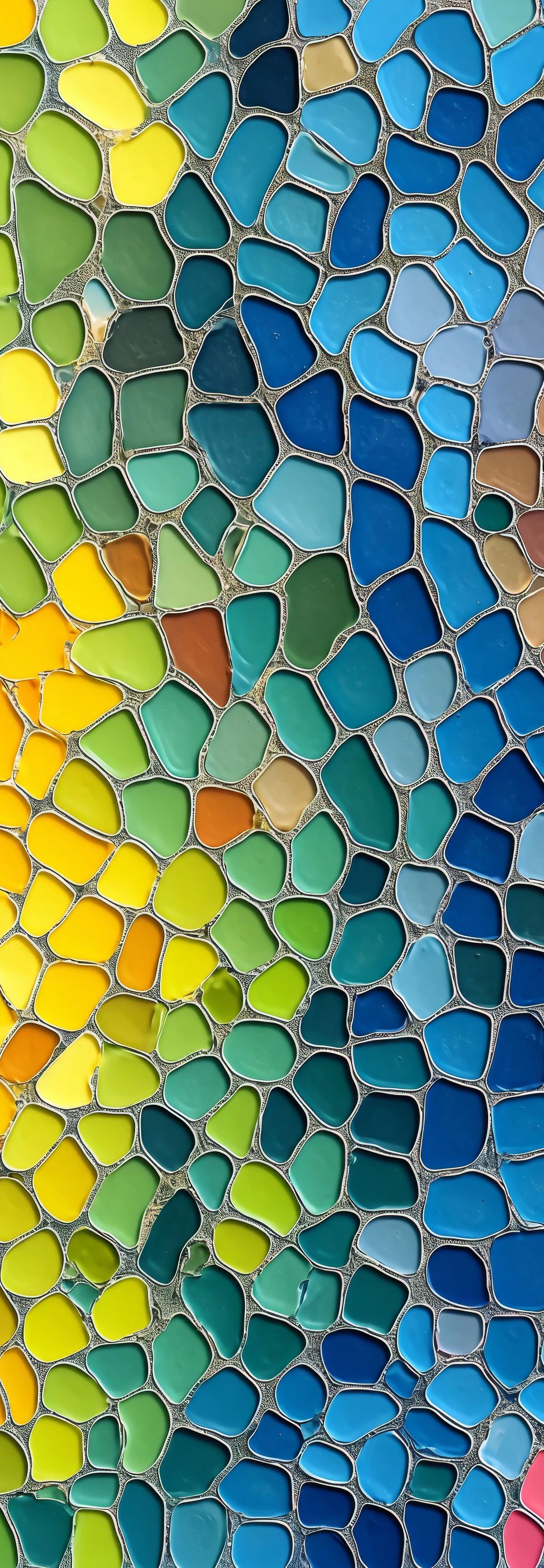 A mosaic of colorful glass tiles with irregular shapes arranged in a rainbow gradient pattern, transitioning from red through orange, yellow, green, blue, and pink